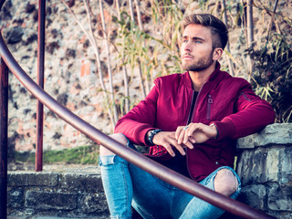 Wall Mural - Handsome young man outdoor in winter fashion, wearing red jacket and woolen scarf in city park