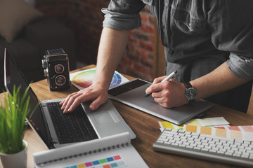 Young creative artist of web design in hat with graphic tablet in modern loft office
