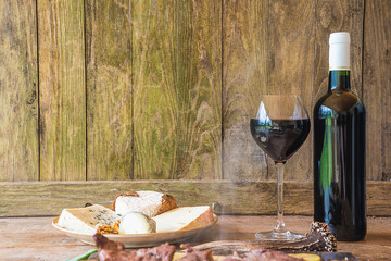 Wall Mural - Bottle and glass of red wine, hot meat and plate with cheeses on rustic wooden background