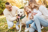 Fototapeta Las - Happy beautiful family with dog labrador is having fun  are sitting on green grass in park.