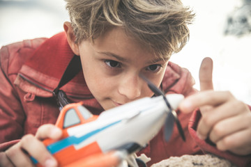 Close up of a little smiling boy playing with a small plane in a sunny day, dreaming about being an airplane pilot. Young and happy kid thinking about planes and pilots. Dreaming to be an aviator.