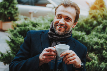 Merry stylish guy is drinking coffee outdoors