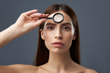 Wall Mural - Charming young lady examining skin with magnifying glass