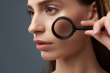 Wall Mural - Beautiful young woman with perfect skin using magnifying glass