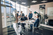 © alfa27 - Multi-ethnic group of business partners of various ages and ethnicities gathered for meeting to discuss details of company expansion to the east - viewed through transparent glass wall.