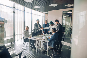 Multiracial team of business partners of different age interacting in boardroom of modern spacious and well-lit office, being viewed through transparent glass wall.