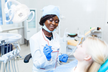 Wall Mural - Female black dentist in dental office talking with female patient and preparing for treatment.