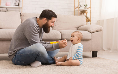 Wall Mural - Father feeding his cute baby son at home