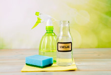 Chemical Free Home Cleaner Products Concept. Using Natural Destilled White Vinegar In Spray Bottle To Remove Stains. Tools On Wooden Table, Green Bokeh Background, Copy Space.