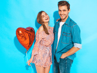 Wall Mural - Portrait of Smiling Beautiful Girl and her Handsome Boyfriend holding  heart shaped air balloons and laughing. Happy Family. Love. Happy Valentine's Day. Posing on blue wall