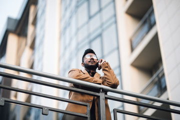 Wall Mural - Young indian man professional worker in suit talking on mobile phone while standing outdoors against skyscraper