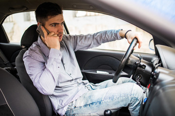 The perfect day for driving. Side view of cheerful young man driving his car and talking on the mobile phone