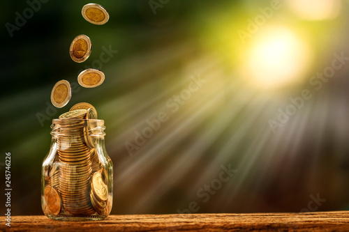 Fotografía Coin in the bottle and drop with growing is savings money put on the wood in the morning sunlight, Business investment and saving growth concept