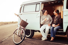 Adult Aged Caucasian Happy Couple Sit Down Out Of A Vintage Van Drinking A Tea And Enjoying The Outdoor Leisure Activity During Travel Vacation - Bike Parked Near The Vehicle