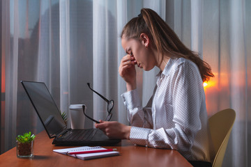 Feeling sick and tired. Frustrated woman massaging nose and keeping eyes closed while sitting at working place. Hard and sedentary work. Need for rest