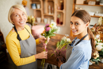 High angle portrait of two female florists looking at camera and smiling while working in flower shop, copy space