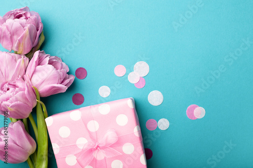 Gift box wrapped in polka dot paper and pink tulip flowers on blue background...