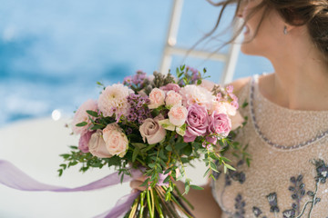 Wall Mural - the bride holds a pink and lilac wedding bouquet in her arms against the background of the sea