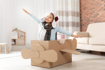 Poster - Cute little girl playing with cardboard airplane in living room