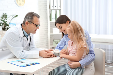 Canvas Print - Young woman with daughter visiting doctor in hospital. Checking pulse