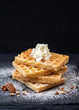 Close-up of sweet tasty Belgian waffles, sprinkled with powdered sugar, pecans, with whipped cream