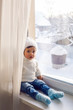 © saulich84 - boy in a white sweater standing at the window on the windowsill