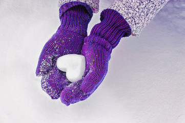 Female hands in knitted mittens with heart of snow in winter day. Love concept. Valentine day background.