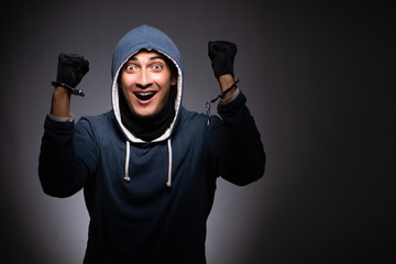 Young gangster in hood on grey background 