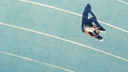 Wall Mural - Sprinter sitting on athletic track. Top view of a female runner sitting on race track in a stadium with shadow falling on the side.