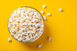 Glass bowl with salted popcorn on yellow background. Top view with copy space. Flat lay