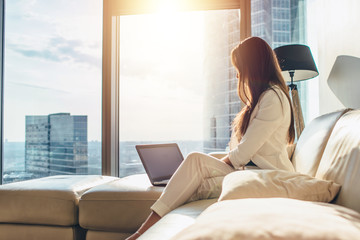 Elegant young female business woman using a laptop sitting on a sofa at home