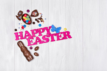 Canvas Print - Pink text of happy easter and chocolate traditional sweets as bunny and eggs