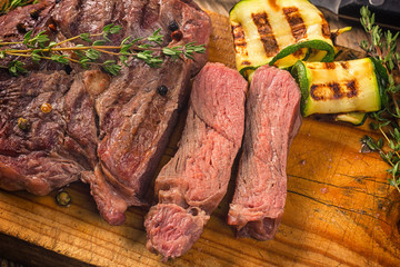 Juicy medium rare beef steak slices on wooden board with herbs spices and salt.