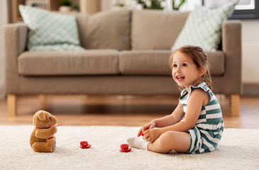 Wall Mural - childhood and people concept - happy three years old baby girl playing tea party with toy crockery and teddy bear at home