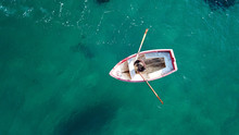 Aerial Drone Bird's Eye View Of Small Traditional Fishing Boat In Port Of Mykonos In Sapphire Clear Waters, Cyclades, Greece