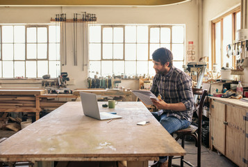 Wall Mural - Woodworker using a laptop and reading notes in his workshop