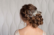 © pushann - Wedding female hairstyle low beam on the head of a brown-haired girl back view on a light background.