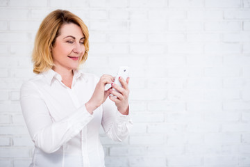 Wall Mural - portrait of cheerful mature business woman using smart phone over white wall