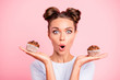 Close-up portrait of nice lovely cute attractive amazed scared afraid girl holding in hands two cakes choosing deciding dilemma opened mouth isolated over pink pastel background