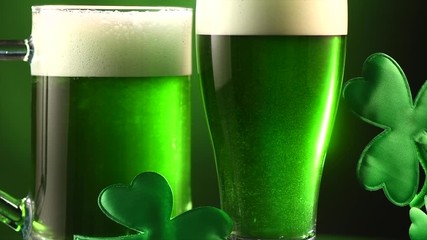 Wall Mural - St. Patric's Day green beer pouring over deep green background, decorated with shamrock leaves. Pint of green beer closeup. Slow motion, 4K UHD video 3840x2160