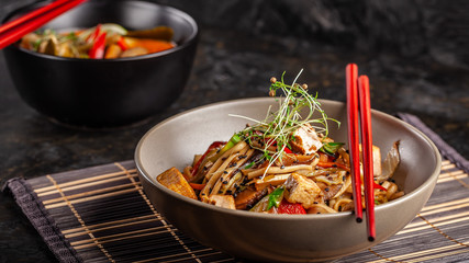 The concept of Japanese cuisine. Chinese noodles with chicken, grilled vegetables, and tofu in unagi sauce. Serving Asian dishes in the restaurant in a plate on a bamboo mat. Top view, copy space