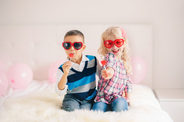 Wall Mural - Group portrait of two happy white Caucasian cute adorable funny children eating heart shaped lollipops. Boy and girl celebrating Valentine Day. Love, friendship and fun. Best friends forever.