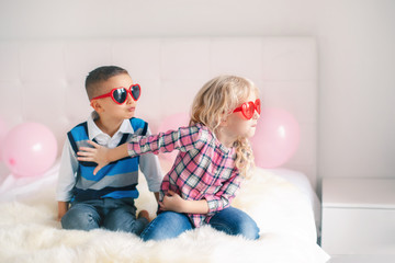 Wall Mural - Portrait of two unhappy white Caucasian cute adorable funny children wearing heart shape glasses. Boy and girl fighting and having a quarrel or misunderstandingl. Love, friendship and hate.