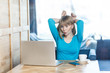 © khosrork - Happy childish young girl freelancer with blonde hair in blue t-shirt are sitting in cafe and making video call on laptop, talking and teased with her friend, holding hands near head like bunny ears.