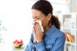 © nenetus - Unhealthy young woman sneezing in a tissue in the living room at home.