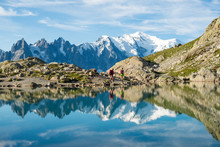 Hikers And The Summit Of Mont Blanc Reflected In Lac Blanc On The Tour Du Mont Blanc Trekking Route In The French Alps, Haute Savoie, Auvergne-Rhone-Alpes, France