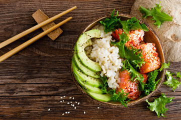 Hawaiian poke coconut bowl with grilled salmon fish, rice and avocado. Healthy food. Top view