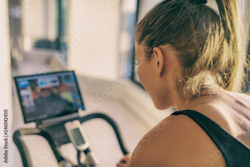 Obraz Dibond Inteligentny ekran rowerowy do ćwiczeń w domu z ćwiczeniami online dla kobiet trenujących na stacjonarnym sprzęcie rowerowym do ćwiczeń rowerowych. Kolarstwo halowe. Skoncentruj się na pocie na plecach osoby.