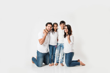 Wall Mural - happy Indian family of 4 standing isolated over white background. Young couple with kids wearing white top and blue jeans. selective focus
