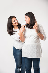 Indian old mother with young Daughter standing isolated over white background, while wearing white top and blue jeans. selective focus